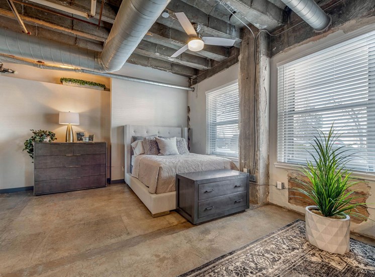 Furnished industrial bedroom with cement floors, ceiling fan, bed and two dressers